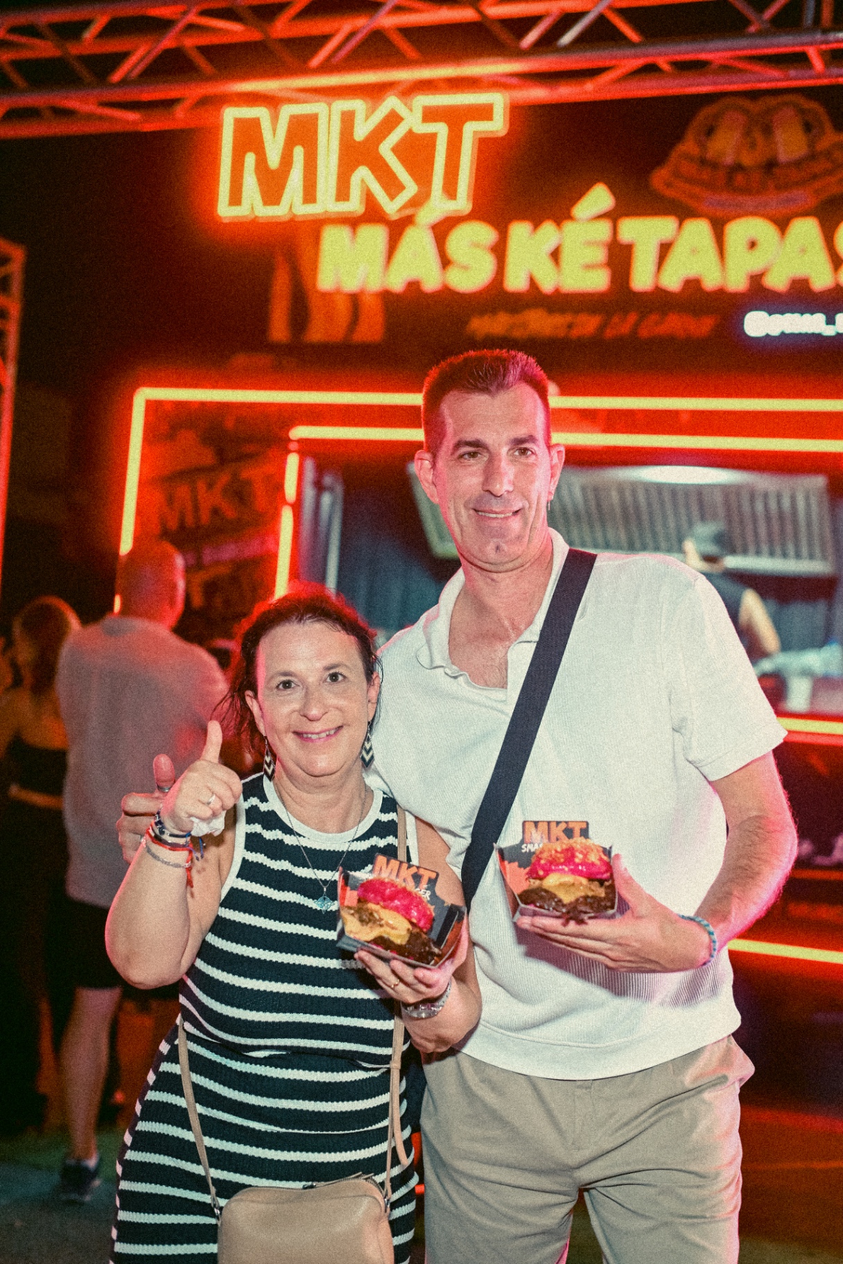 Pareja de clientes sonriendo con dos smash burgers MKT delante de la foodtruck